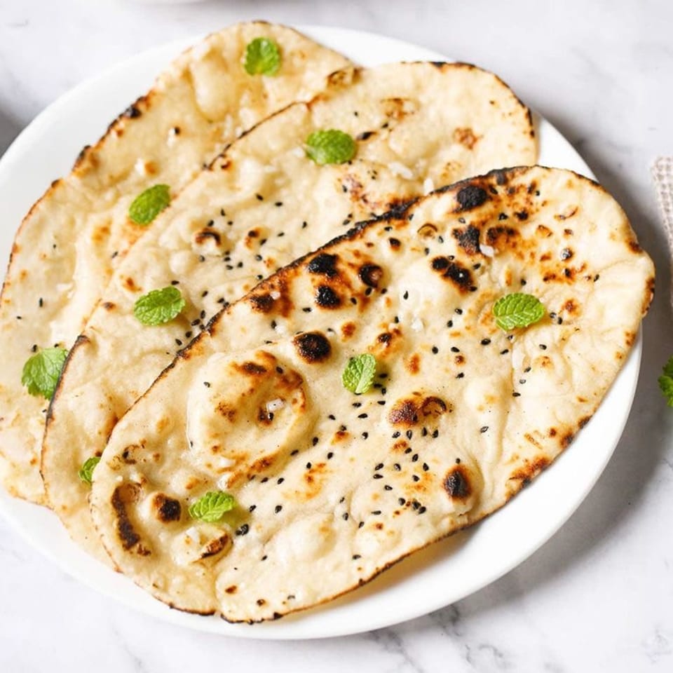 Garlic Naan with charred spots and herb garnish.